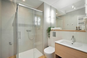 Een moderne badkamer met een douchecabine van glas, een wit toilet en een wastafel met houten kastje.