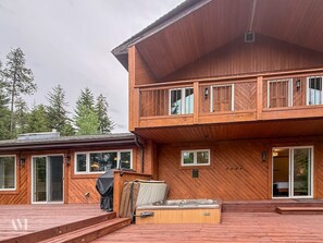 Ein zweistöckiges Holzhaus mit einer Terrasse, großen Fenstern und einem Eingang mit Glastür.