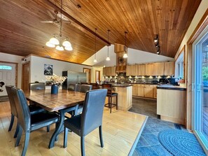 Cozinha moderna com armários de madeira, área de refeições com mesa e cadeiras de madeira, e uma ilha grande.