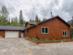 Eine Holzhütte mit Garage, umgeben von Kies und Bäumen.