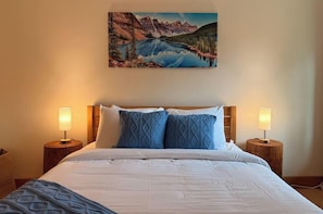 Ein Bett mit weißer Bettwäsche, zwei blaue Kissen mit Muster und einem Holzkopfstück.