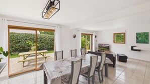 Ein Essbereich mit Tisch, Stühlen, einem Fernseher und Blick auf einen Garten durch eine Schiebetür.