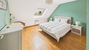 Ein Schlafzimmer mit Bett, Nachttischen, einem Sessel, einem Schreibtisch, einem Fenster und einer Deckenleuchte.
