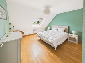 Ein Schlafzimmer mit Bett, Nachttischen, einem Sessel, einem Schreibtisch, einem Fenster und einer Deckenleuchte.