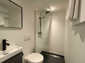 Een moderne badkamer met een douchecabine van glas, een wit toilet, een zwarte kraan en een spiegel boven de wasbak.