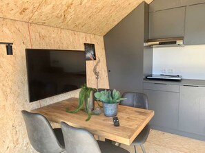 Een kleine keuken met een houten eettafel, stoelen, een televisie en een plant in pot.
