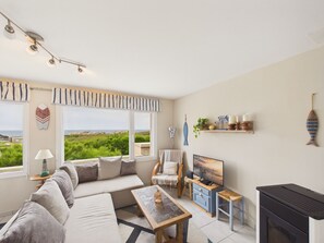 Ein Wohnzimmer mit Sofa, Fernseher, Kamin und Meerblick.