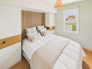 A bedroom with a bed, wooden headboard, white bedding, a window with a view, and a hanging light fixture. - House with sea views – 300 m from the harbour (Penmarch)