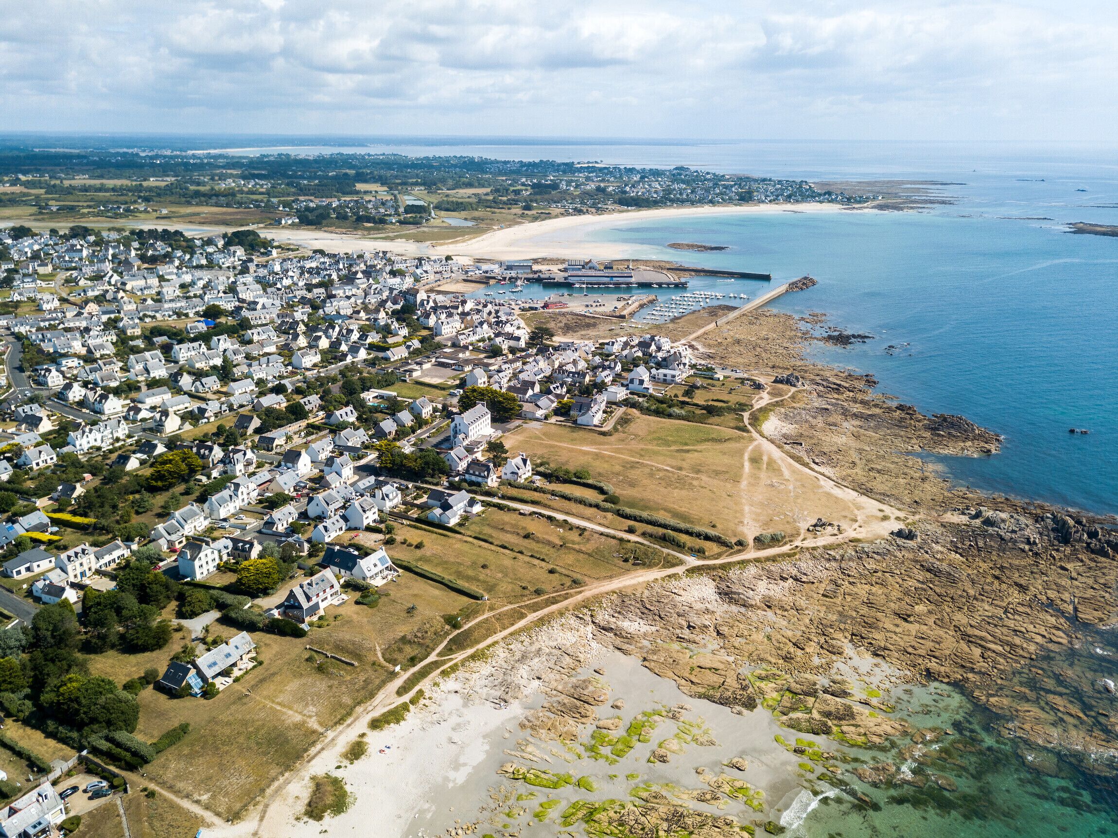 Vue aérienne d’une zone résidentielle côtière, avec des maisons, une plage et un port de plaisance.
