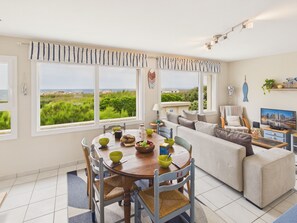 Ein Essbereich mit Meerblick, ein Wohnzimmer mit Sofa und Fernseher sowie eine Küchenzeile.