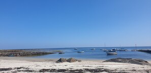 Ein Strand mit Booten, Felsen und blauem Himmel.