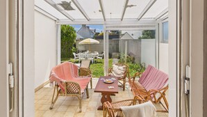 Een overdekt terras met rieten meubels, een tafel en een glazen deur naar een tuin.