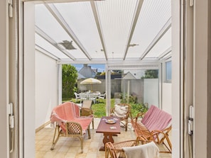 Ein überdachter Patio-Bereich mit Korbmöbeln, einem Tisch und einer Glastür, die in einen Garten führt.