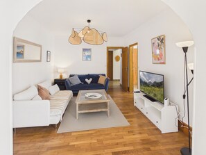 Ein Wohnzimmer mit einer Couch, einem Couchtisch, einem Fernseher und einer Deckenleuchte.