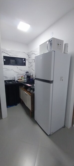 A compact kitchen with a refrigerator, microwave, and stove. - Cozy studio in the city center. (Armação dos Búzios)