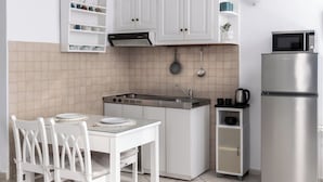 A compact kitchen with white cabinetry, a stainless steel refrigerator, and a dining table with white chairs. - Folia Bianca-Mi Amo (Imerovigli)
