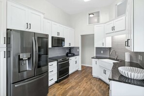 A modern kitchen with white cabinetry, stainless steel appliances, and a black countertop. - Step-Free Family Home with BBQ in Montgomery (Montgomery)