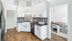 Una cocina moderna con armarios blancos, encimera negra y comedor con mesa y sillas.