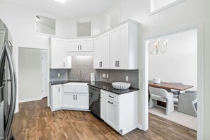 A modern kitchen with white cabinets, a black countertop, and a dining area with a table and chairs. - Step-Free Family Home with BBQ in Montgomery (Montgomery)