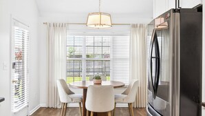 Una cocina moderna con un refrigerador de acero inoxidable, una mesa redonda con cuatro sillas y una ventana con persianas.