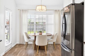 A modern kitchen with a stainless steel refrigerator, a round dining table with four chairs, and a window with blinds. - Step-Free Family Home with BBQ in Montgomery (Montgomery)