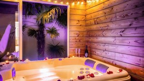 Une cabane en bois avec un jacuzzi, des plantes tropicales et des bougies.