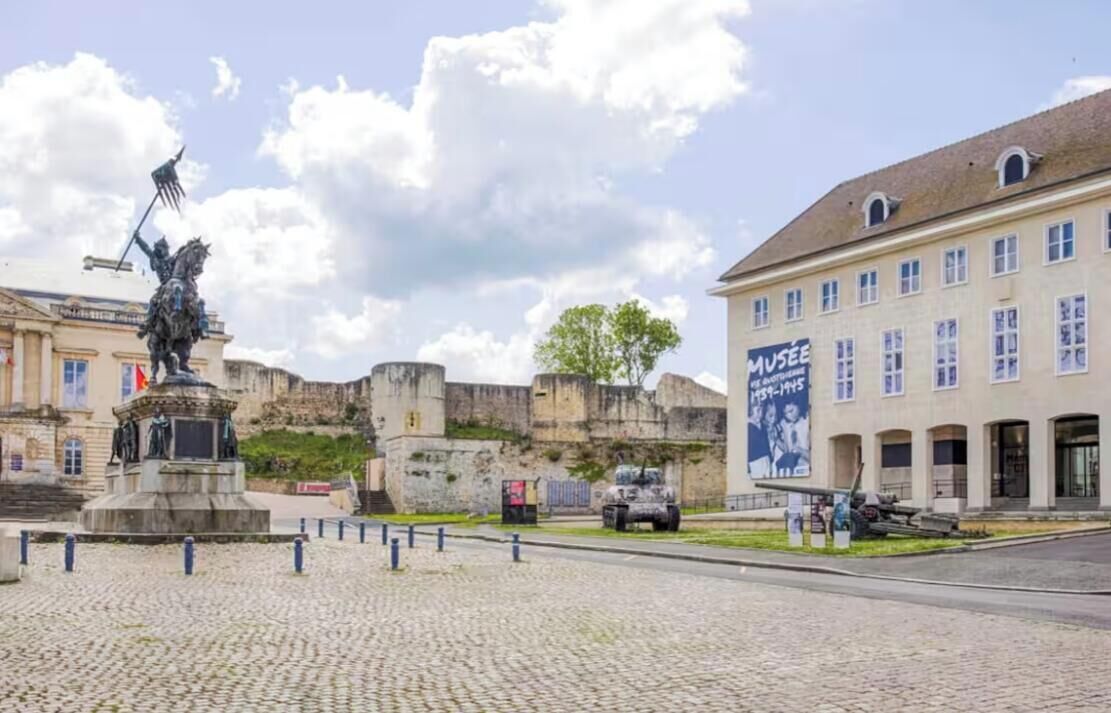 Ein Pflasterplatz mit einer Statue, einem Museumsgebäude und einer historischen Mauer.