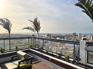 A rooftop terrace with a view of the cityscape, a seating area, and potted plants.