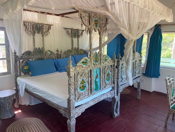 A four-poster canopy bed with intricate carvings and a white canopy, blue pillows, and a decorative headboard.