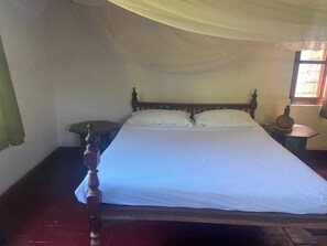 A single bed with a wooden headboard, a bedside table with a lamp, and a window with curtains.
