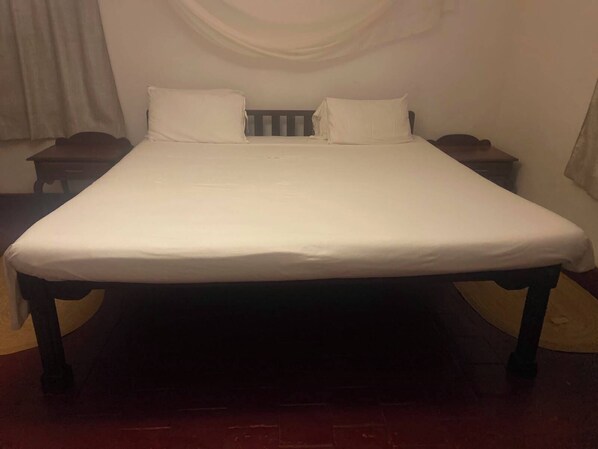 Una cama estándar con colchón y almohadas blancas, flanqueada por dos mesitas de noche de madera con acabados oscuros.