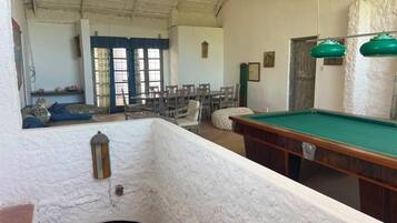 A billiards table, chairs, and a small pool table in a room with a high ceiling and white walls.