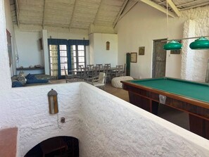 A billiards table, chairs, and a small pool table in a room with a high ceiling and white walls.