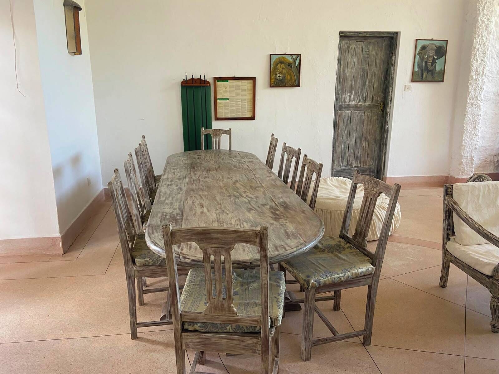 Un comedor con una mesa de madera larga y sillas, un tablón de anuncios verde y una puerta de madera.