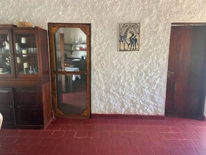 Una habitación con piso de ladrillo, un mueble de madera con puertas de cristal, una puerta de madera y un cuadro colgado en la pared.