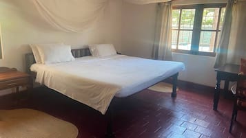 Quarto com cama, mesa de cabeceira de madeira, tapete tecido e janela com cortinas.