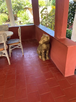En terrasse med et træbord og stole, røde fliset gulv og en bjørn statue.