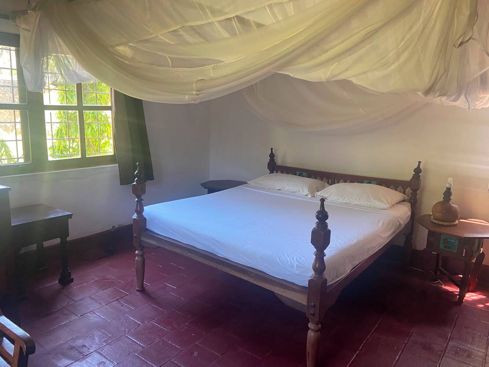 Ein Zimmer mit Himmelbett, kleinem Tisch, Nachttisch und einem fenster mit Vorhängen.