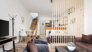 Una sala de estar moderna con televisor, sofás, una mesa de centro y una escalera que lleva a un dormitorio.