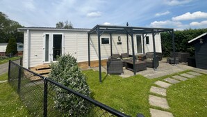 A mobile home with a covered patio area, outdoor seating, and a fenced yard. - Cozy Beach Stay With Climate Control (Kamperland)