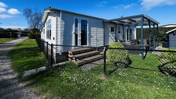 A single-story mobile home with a covered porch and a fenced yard. - Cozy Beach Stay With Climate Control (Kamperland)