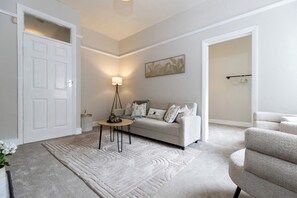 Ein Wohnzimmer mit einer Couch, einer Lampe, einem Teppich und einem Gemälde an der Wand.