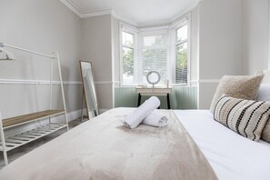 A neatly arranged bedroom with a bed, a bedside table, a mirror, and a window with blinds. - Gateshead 2BR Flat - Near Town & Metro Access (Tyne and Wear)