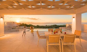 A rooftop terrace with a dining table, chairs, and a view of the sea at sunset. - Marea Maxima Villa 2 Heated Pools (Dramia)