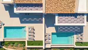 Eine Vogelperspektive eines Resorts mit zwei Schwimmbecken, Liegestühlen und einem gepflasterten Dach.