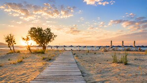Ein Holzweg, der zu Strandstühlen und Sonnenschirmen führt.