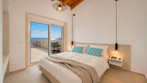 Ein Schlafzimmer mit Bett, Nachttisch, Lampe und Meerblick durch eine Glastür.