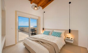 A bedroom with a bed, a nightstand, a lamp, and a view of the sea through a glass door. - Marea Maxima Villa 2 Heated Pools (Dramia)