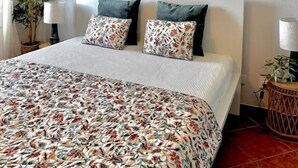 Ein Schlafzimmer mit einem Bett, einem runden Spiegel, zwei Topfpflanzen und einer Lampe.
