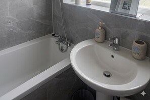 A bathroom with a bathtub, a sink, and a window. - Spacious 3BR Flat Sleeps 7 in Greenford (London)